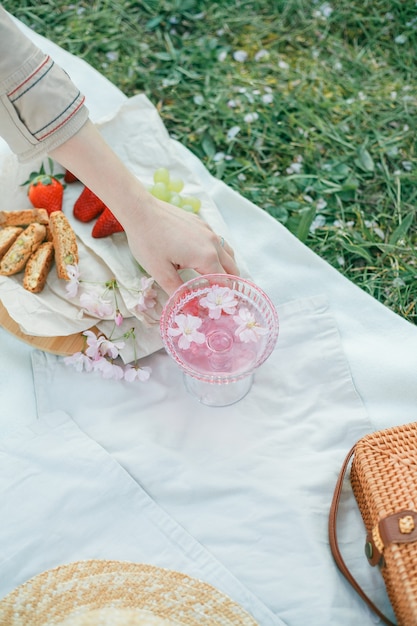 Piquenique da primavera na natureza. Uma taça de champanhe rosa com flores de sakura, uma bolsa de vime, um chapéu, italiano. Vinho. Primavera.