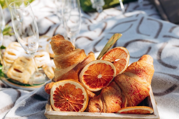 Piquenique de verão ao ar livre em dia ensolarado com placa de corte de madeira croissant, copo de vinho e cobertor marrom Estilo aconchegante rústico