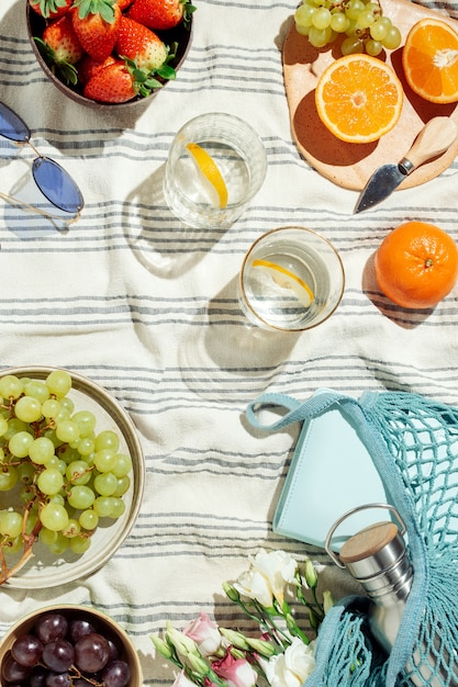 Piquenique de verão feminino flatlay, frutas, bagas e água de limão em cobertor de algodão listrado