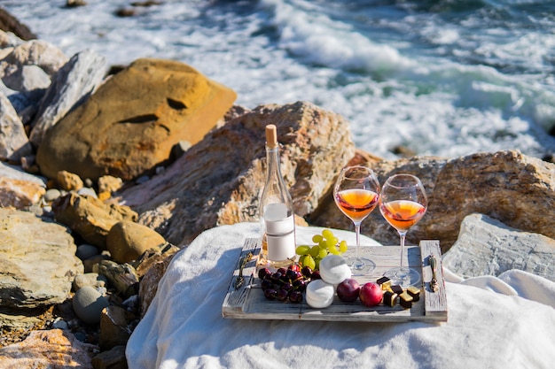 Piquenique do verão da cena do mar da praia com vinho cor-de-rosa e uvas, marshmallow, bagas.