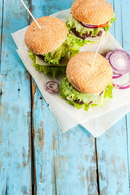 Piquenique, Fast-food. Alimentos não saudáveis. Deliciosos hambúrgueres saborosos frescos com costeleta de carne, legumes frescos e queijo na velha mesa de madeira azul rústica com água com gás. vista do topo