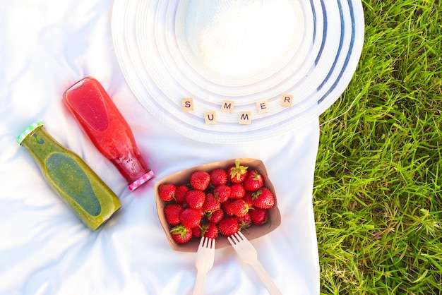 Piquenique no parque com morangos smoothies chapéu de verão e margaridas em uma grama verde Almoço ao ar livre