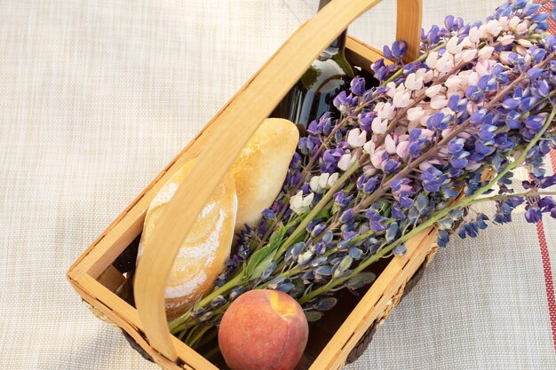 Piquenique romântico para um casal. Cesta com flores, vinho, pêssegos e baguetes em um fundo de grama brilhante de verão, vista de cima