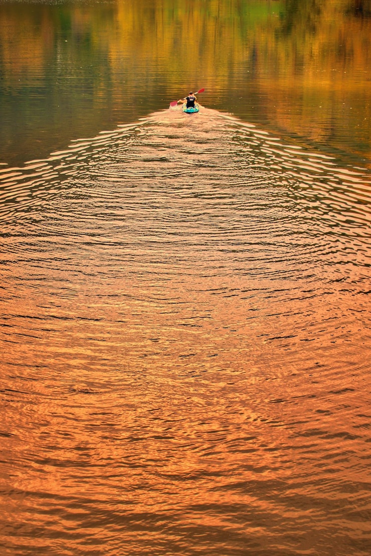 Foto un piragüista remando en un lago al amanecer dejando tras de sí una estela en el agua.