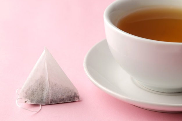 Pirámide de bolsita de té y taza con té sobre un delicado fondo rosa. para hacer té.