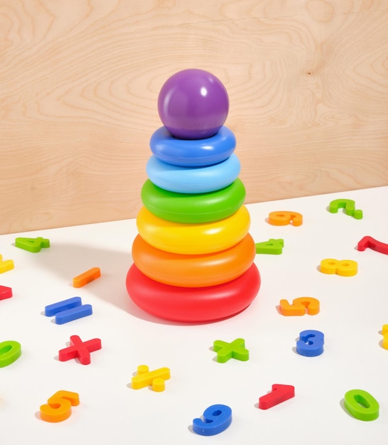 Pirâmide de brinquedo para crianças com anéis multicoloridos e uma bola roxa no topo Números multicoloridos espalhados pela superfície