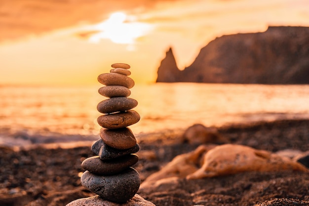 Pirâmide de seixos equilibrada na praia em um horário de pôr do sol ondas do mar e espuma no fundo seletivo