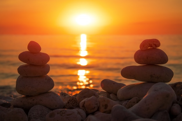 Pirámide de los pequeños guijarros en la playa. Piedras, contra el fondo de la orilla del mar durante el atardecer