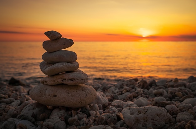 Pirámide de los pequeños guijarros en la playa. Piedras, contra el fondo de la orilla del mar durante el atardecer