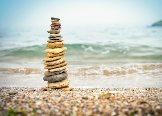 Pirámide de piedras sobre arena que simboliza zen, armonía, equilibrio. Energía positiva. Océano en el fondo