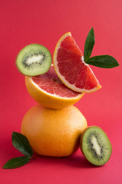 Pirámide de pomelo y kiwi en equilibrio sobre fondo rojo.