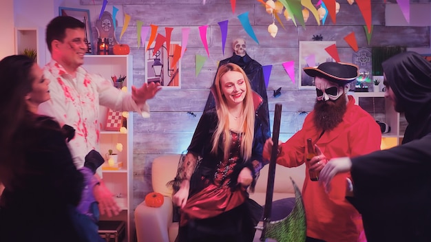 Pirata barbudo com machado e seus amigos dançando na festa de halloween em sala decorada
