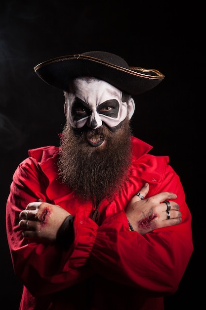 Pirata barbudo mal com maquiagem assustadora para o halloween sobre fundo preto.