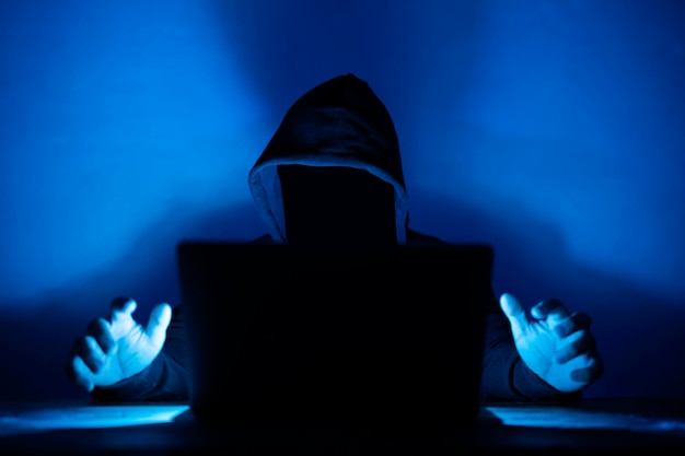 Pirata informático con capucha y rostro oscurecido Pirata informático frente a su computadora Cara oscura