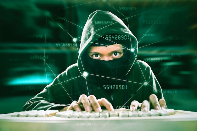 Pirata informático encapuchado escribiendo en el teclado en el ciberespacio