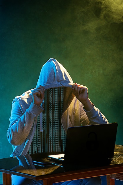 Pirata informático encapuchado robando información con una computadora portátil. Concepto de amenaza