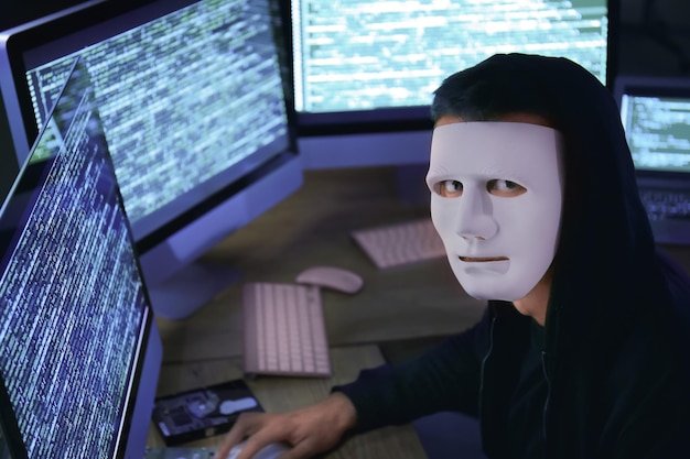 Pirata informático enmascarado usando computadora en cuarto oscuro Amenaza de ataque cibernético