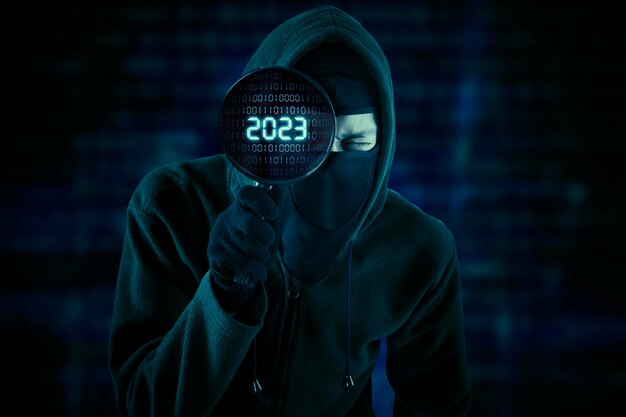 Pirata informático masculino que mira el número 2023 en la lupa