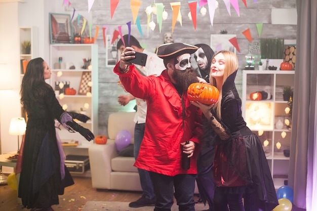 Pirata medieval barbudo tomando uma selfie com uma linda mulher vampira na festa de halloween. Abóbora assustadora.