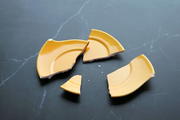 Pires de cerâmica amarela vívida quebrada espalhados na mesa de mármore preto da cozinha