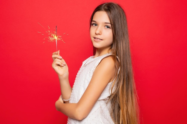 Foto pirotecnia y gente concepto sonriente mujer joven o adolescente mujer feliz con chispas celebrar en vestido blanco sobre fondo rojo mirando a través de su hombro a la cámara