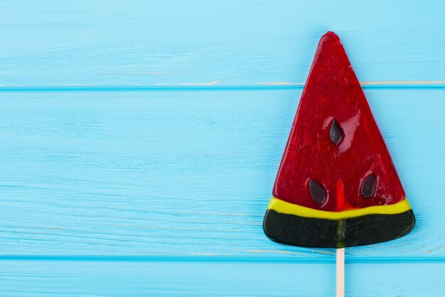 Piruleta de caramelo de sandía sobre fondo azul. Vista frontal de piruleta de sandía con espacio de copia. Dulces saludables para niños.