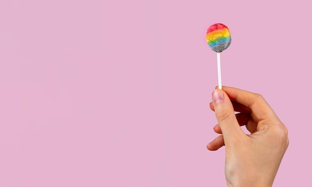 Piruleta de colores del arco iris en la mano en la bandera de fondo rosa