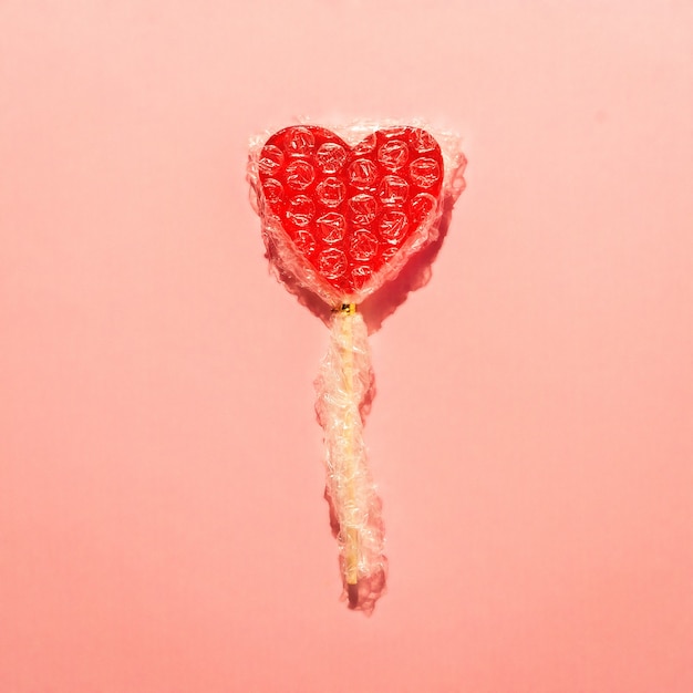 Piruleta de corazón solitario envuelta en plástico de burbujas. Concepto creativo de amor.