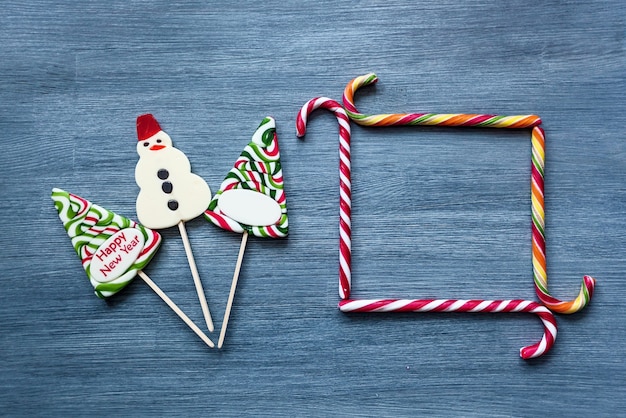 Foto piruletas de caramelo de colores dulces de año nuevo sobre un fondo azul. árbol de navidad, piruletas y muñeco de nieve. dulce lechón, el dulce marco de los palitos de caramelo