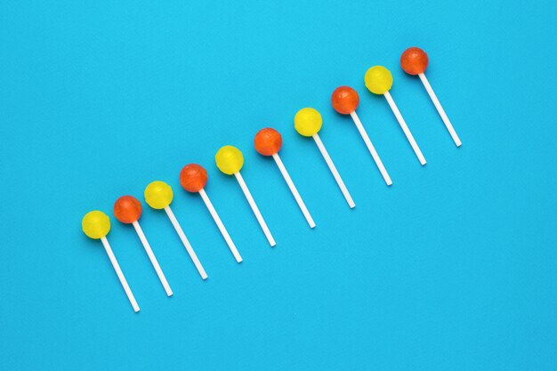 Las piruletas dispuestas en fila en un palo son de color amarillo y naranja sobre un fondo azul Concepto mínimo Caramelos dulces