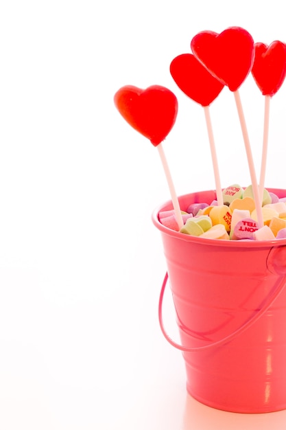 Piruletas de fresa en forma de corazón rojo en cubo rosa.