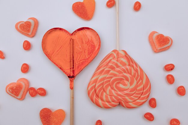 Foto piruletas, mermelada. caramelos gomosos en forma de corazones sobre un fondo blanco. día de san valentín