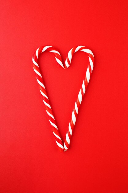 Piruletas de Navidad redwhite apiladas en forma de corazón sobre un fondo rojo Fondo de Navidad
