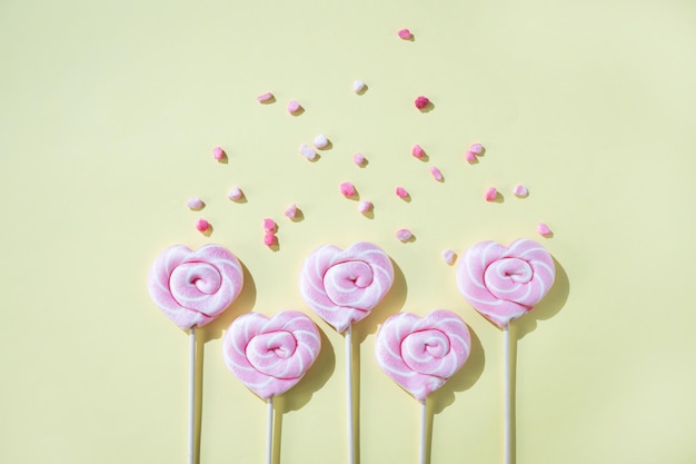 Foto piruletas rosas en forma de corazones con azúcar de color sobre un fondo amarillo vista superior y espacio de copia