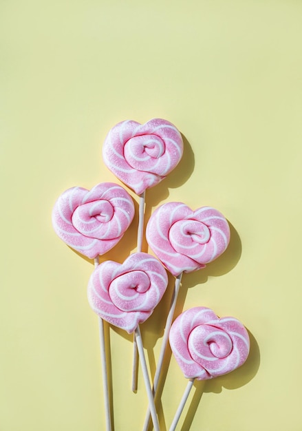 Piruletas rosas en forma de corazones sobre un fondo amarillo Vista superior y orientación vertical del espacio de copia