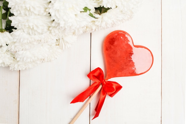 Pirulito do Dia dos Namorados em formato de coração com flores sobre a mesa de madeira