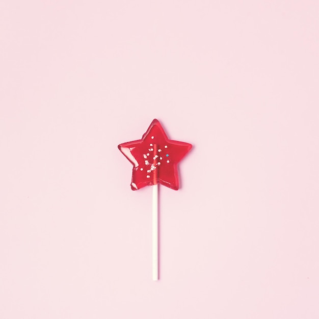 Pirulito em forma de estrela vermelha sobre fundo rosa claro Doce de pirulito de frutas caseiro