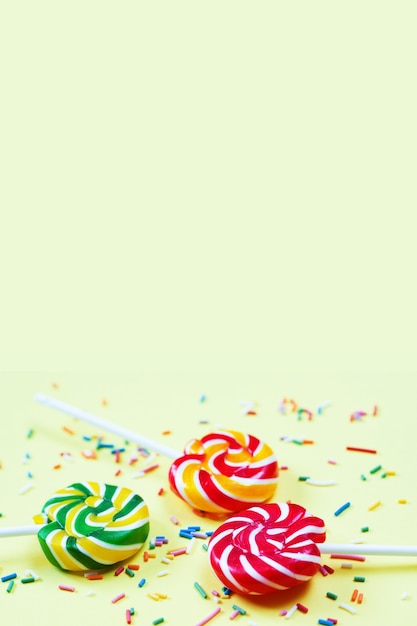 Foto pirulitos coloridos e confetes em fundo amarelo. doces para festa. açúcar