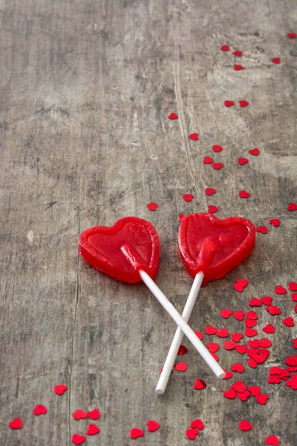 Pirulitos vermelhos com forma de coração na superfície de madeira amam o conceito dia dos namorados.