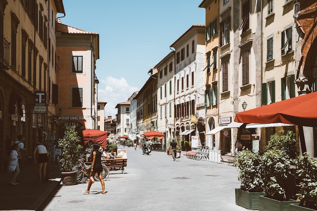 Pisa, Italien - 29. Juni 2018: Zu Fuß auf der Borgo Stretto Straße in Pisa Stadt mit historischen Gebäuden und Geschäften. Die Leute laufen und ruhen sich aus. Sonniger Sommertag und blauer Himmel