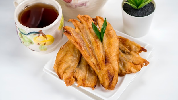 Pisang goreng o buñuelos de plátano tradicional de Indonesia servido en plato blanco con té