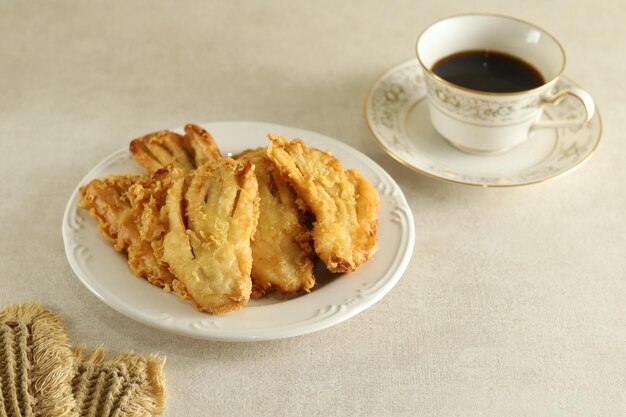 Pisang goreng ou bolinho de banana ou banana frita servem em prato branco com uma xícara de café.