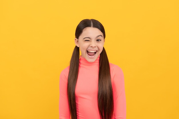 Piscando a criança com cabelo comprido em fundo amarelo, emoções.