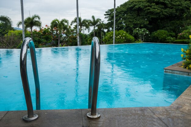 Piscina com barras de apoio escada e árvore.