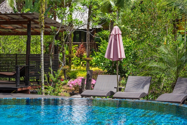 Piscina com espreguiçadeiras relaxantes e guarda-sol em jardim tropical perto da praia na Tailândia