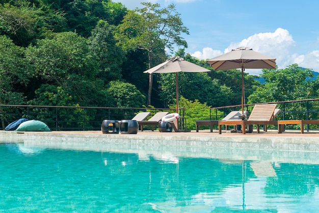 Piscina com guarda-chuva ao redor da piscina com fundo de montanha e céu azul