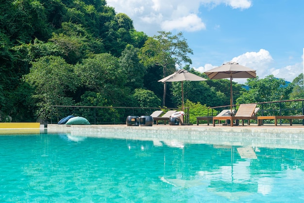 piscina com guarda-chuva ao redor da piscina com fundo de montanha e céu azul