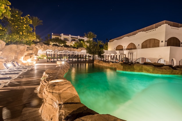 Piscina com iluminação noturna e prédios luxuosos atrás dela