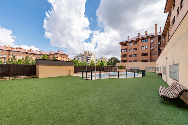 Piscina da urbanização coberta com lona e piso estofado com grama artificial em dia de céu azul e nuvens