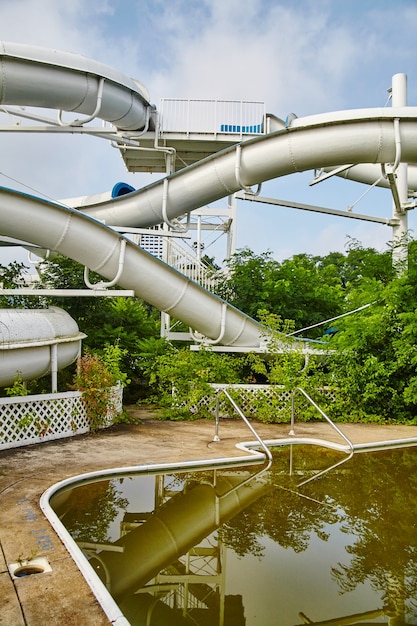 Piscina de água marrom com um enorme toboágua ao fundo em um parque temático abandonado